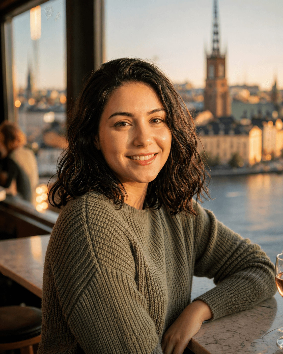 Smiling small-business owner sitting by a Stockholm waterfront window at golden hour