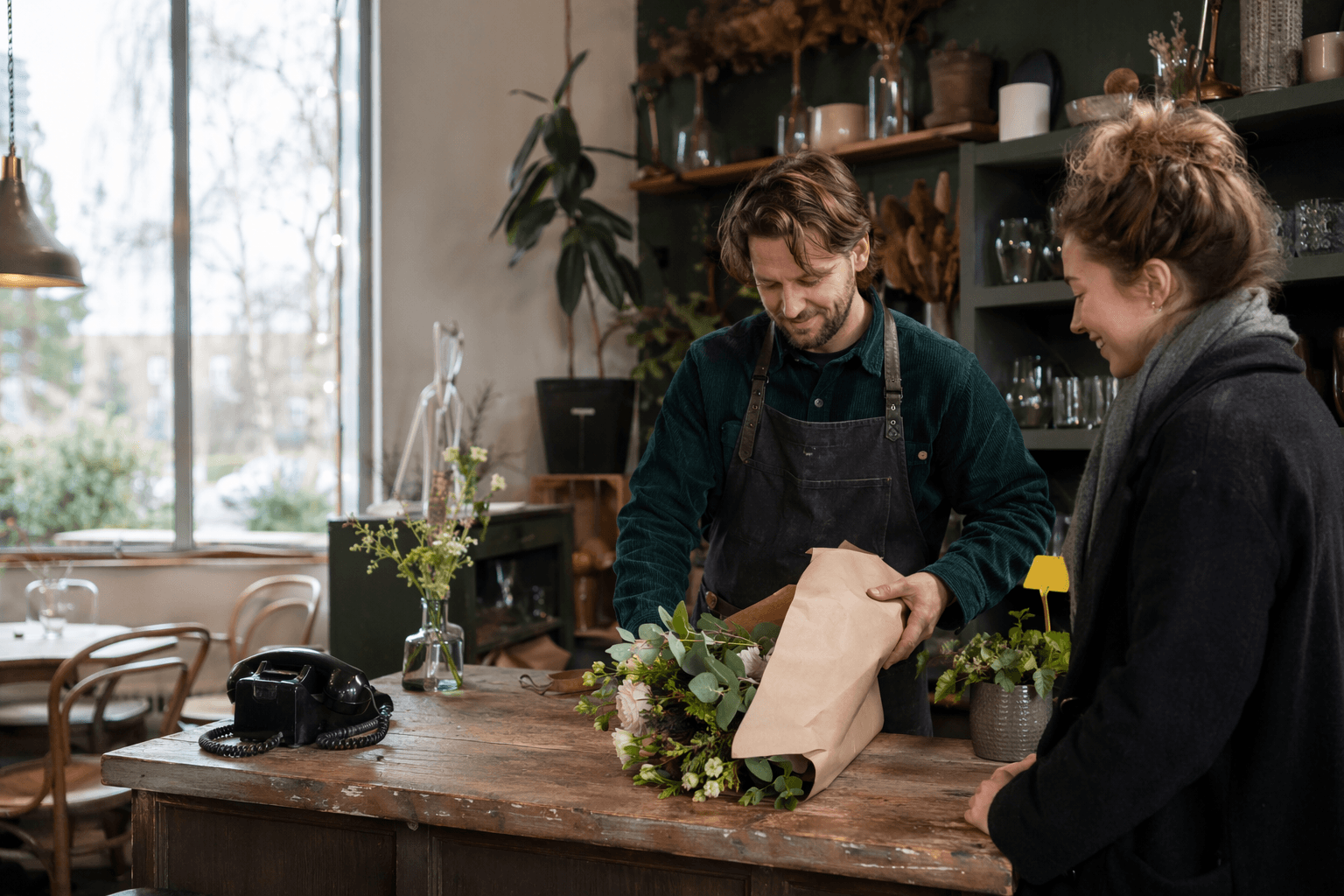 Florist-café owner helping a customer at the counter while the phone sits idle beside her