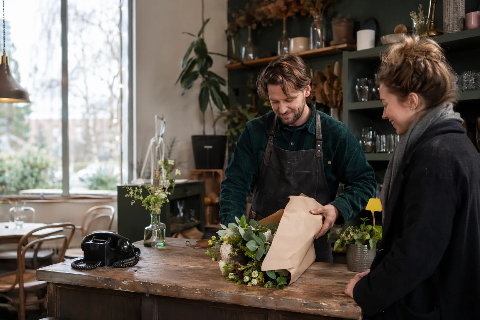 Florist-café owner helping a customer at the counter while the phone sits idle beside her